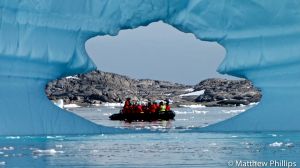 Iceberg with a great hole and a full zodiac passing behind. Lemare Channel, Antarctic Peninsula.